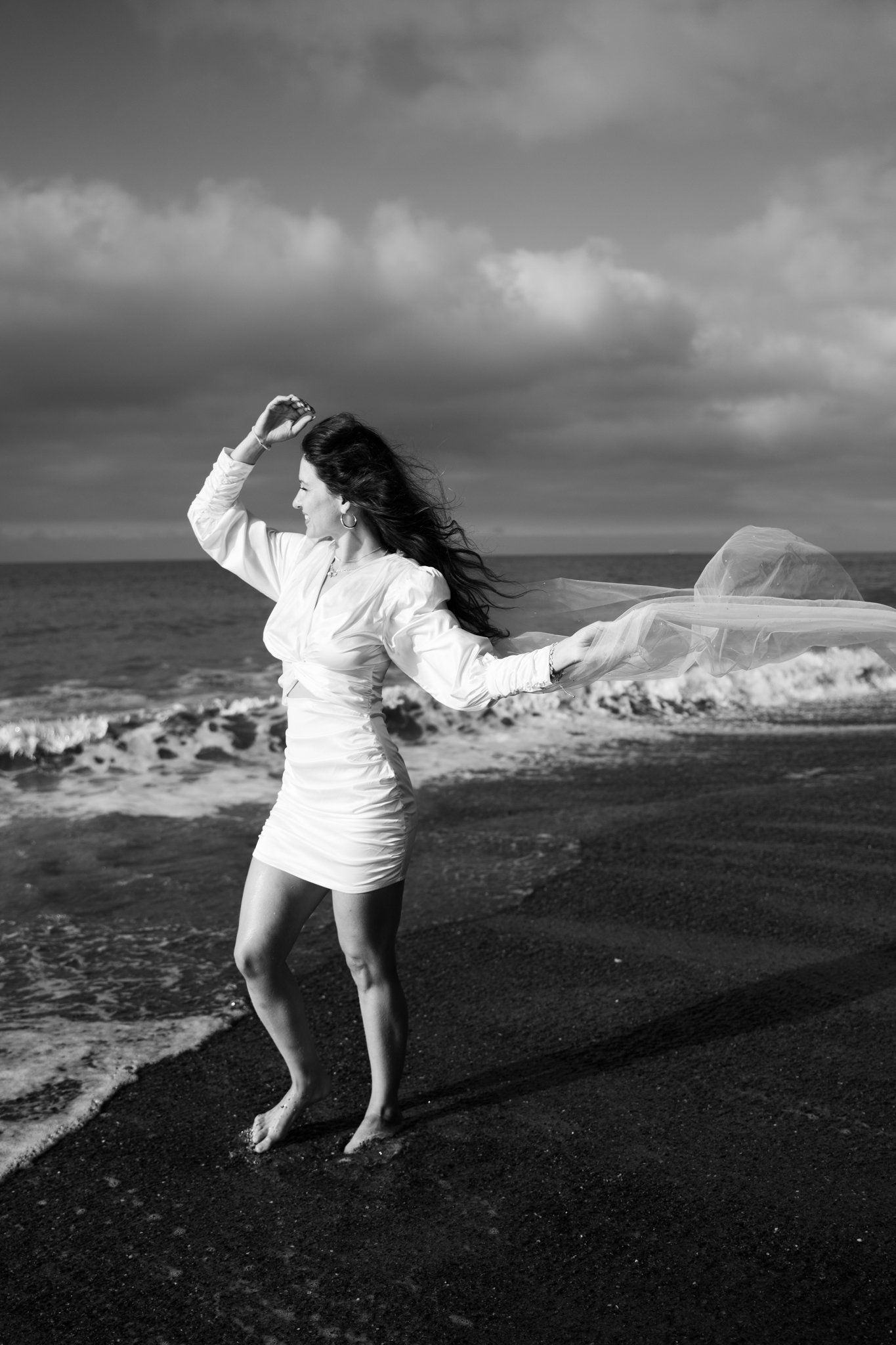 Woman holding up her vail in the wind on beach