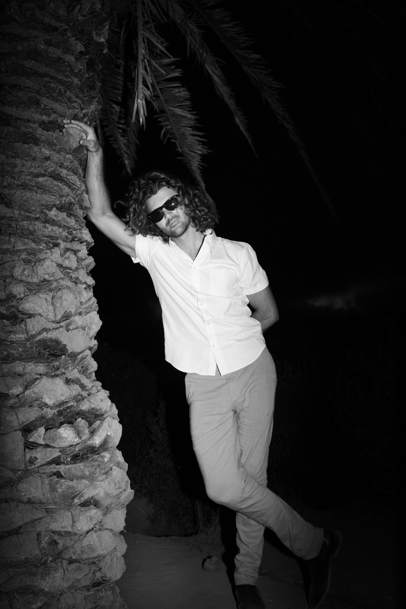 man leaning agianst plamtree with sunglasses