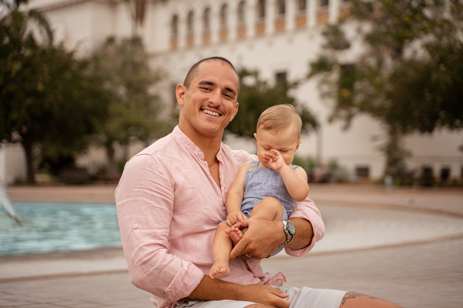 Man smiling in the camera, holding baby in his arms.