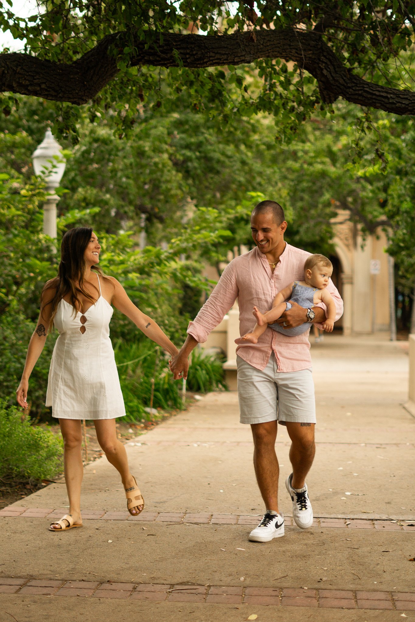 Woman holding Mans hand, baby sitting on sholders from man.