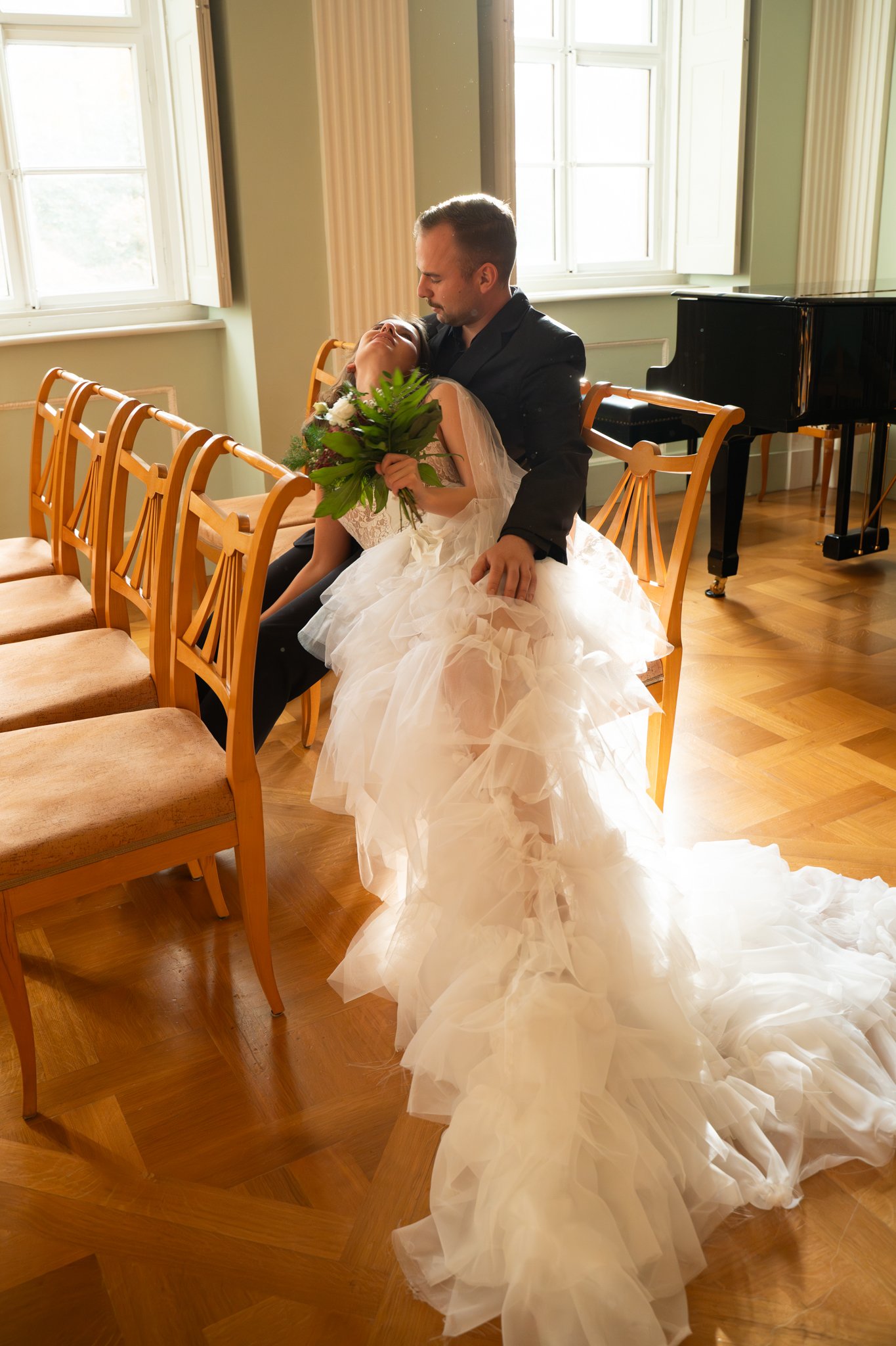 Nick is sitting on chair and clara is leaning over and holding on to her flowers