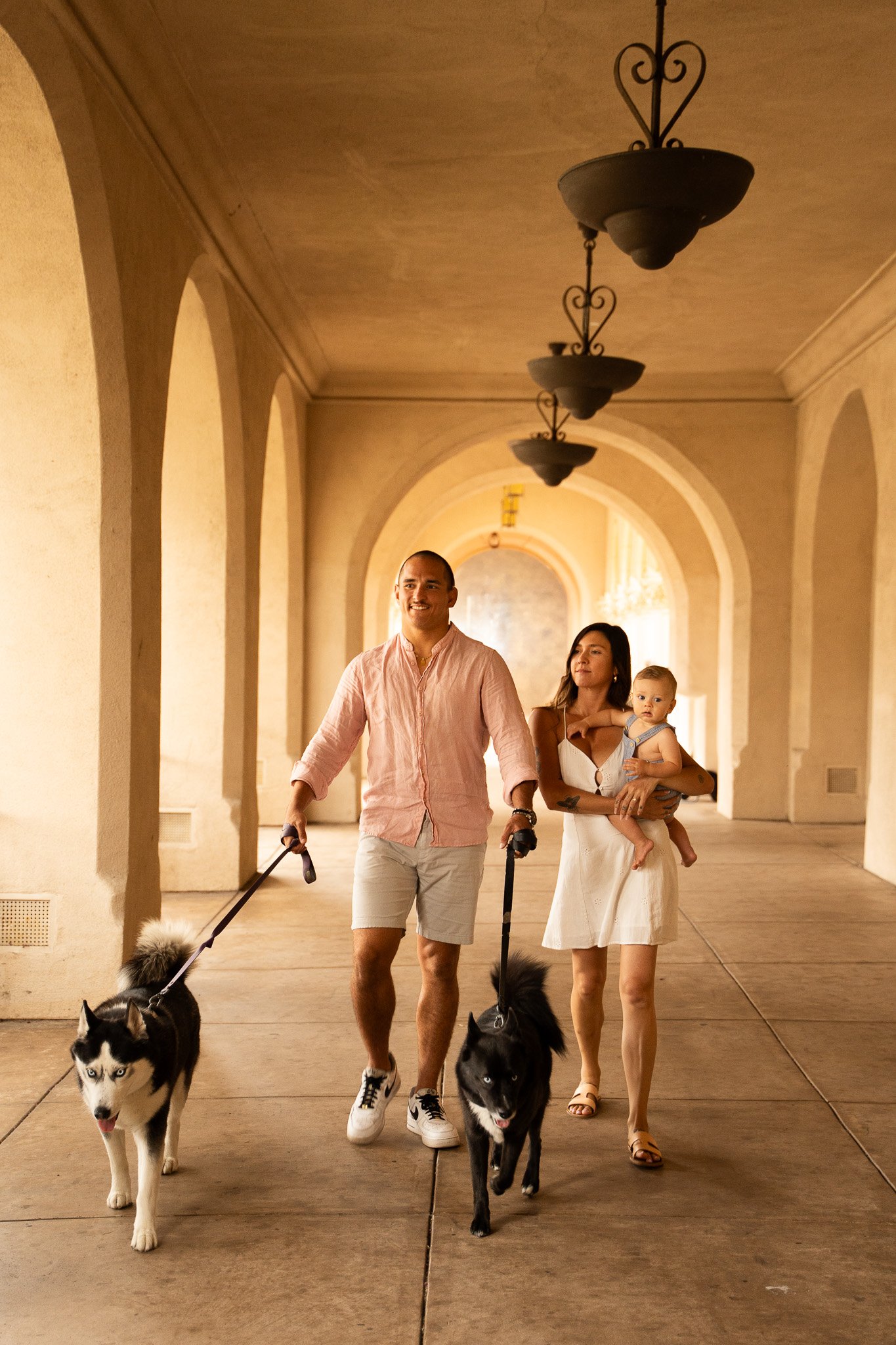 man and woman walking in balboa park, san diego and holding their baby and their dogs.