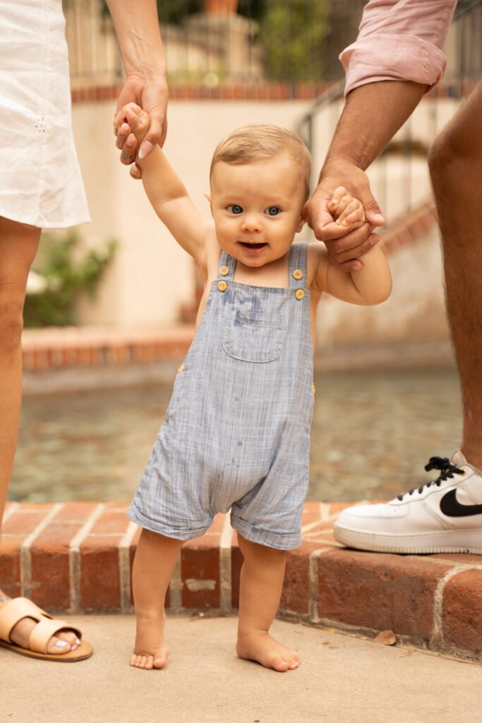 Baby inbetween mother and farther, holding their hands.